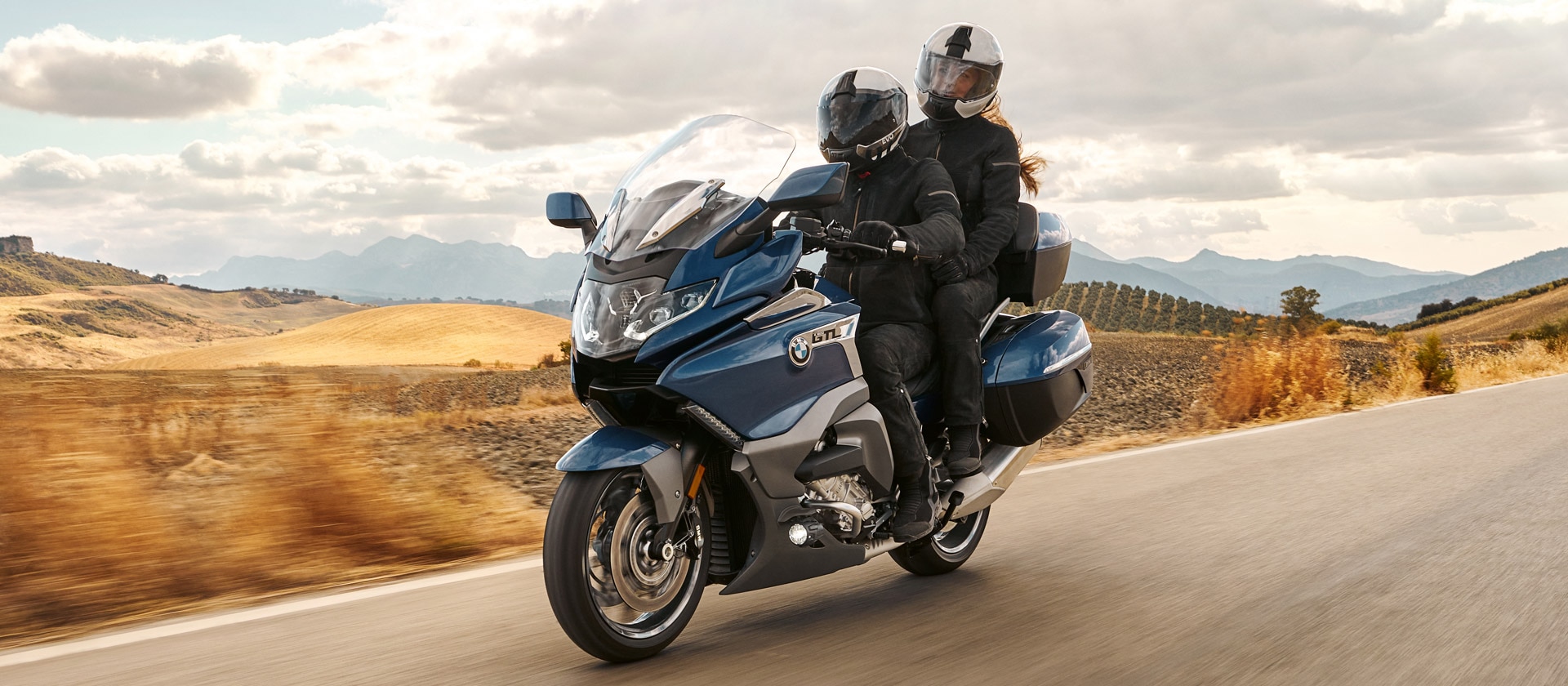 Modelul K 1600 GTL nuanța Gravity Blue cu partener, în mers printr-un peisaj deluros.